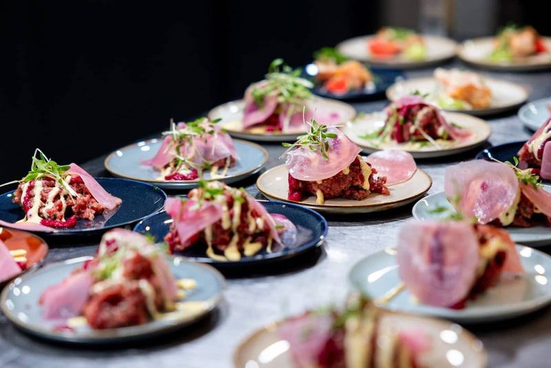 Professionally plated gourmet appetisers with beef tartare, cured meats and microgreens on ceramic plates