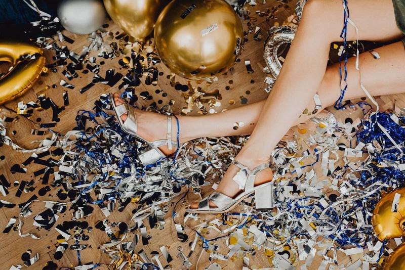 Silver party heels surrounded by gold confetti and balloons on a wooden floor