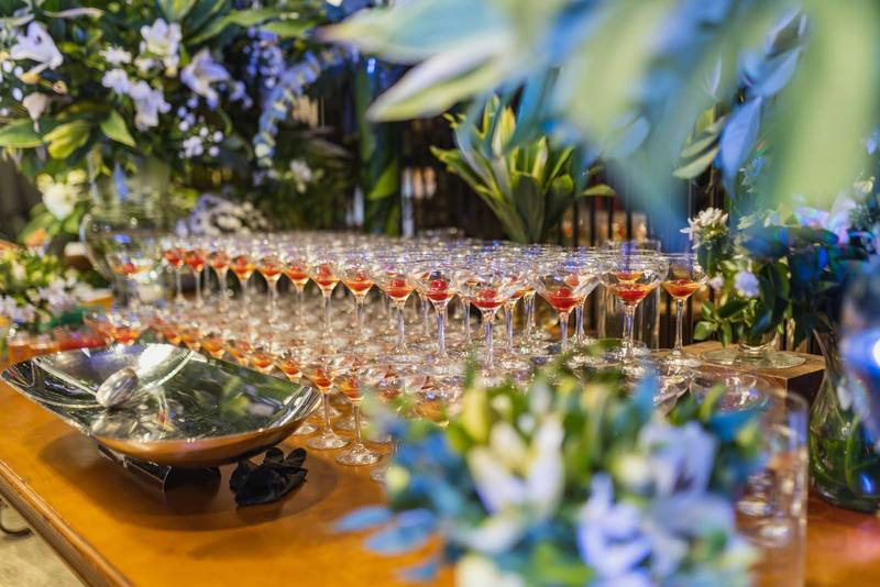 Row of cocktail coupe glasses with drinks surrounded by floral arrangements