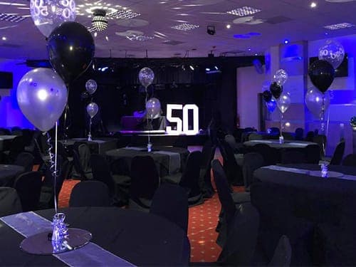 Function room set up for a 50th birthday party with black and silver balloons and illuminated 50 marquee letters