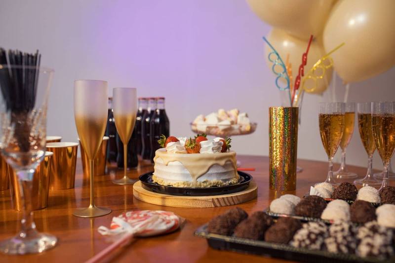 Party table with a cream cake topped with strawberries, champagne flutes, gold balloons and chocolate truffles