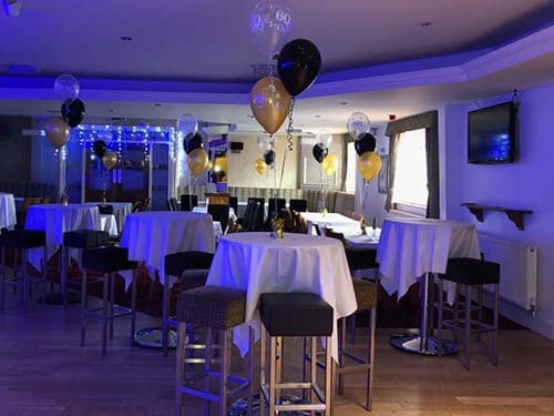 Lounge area set up for a party with high cocktail tables, black and gold balloons and fairy lights